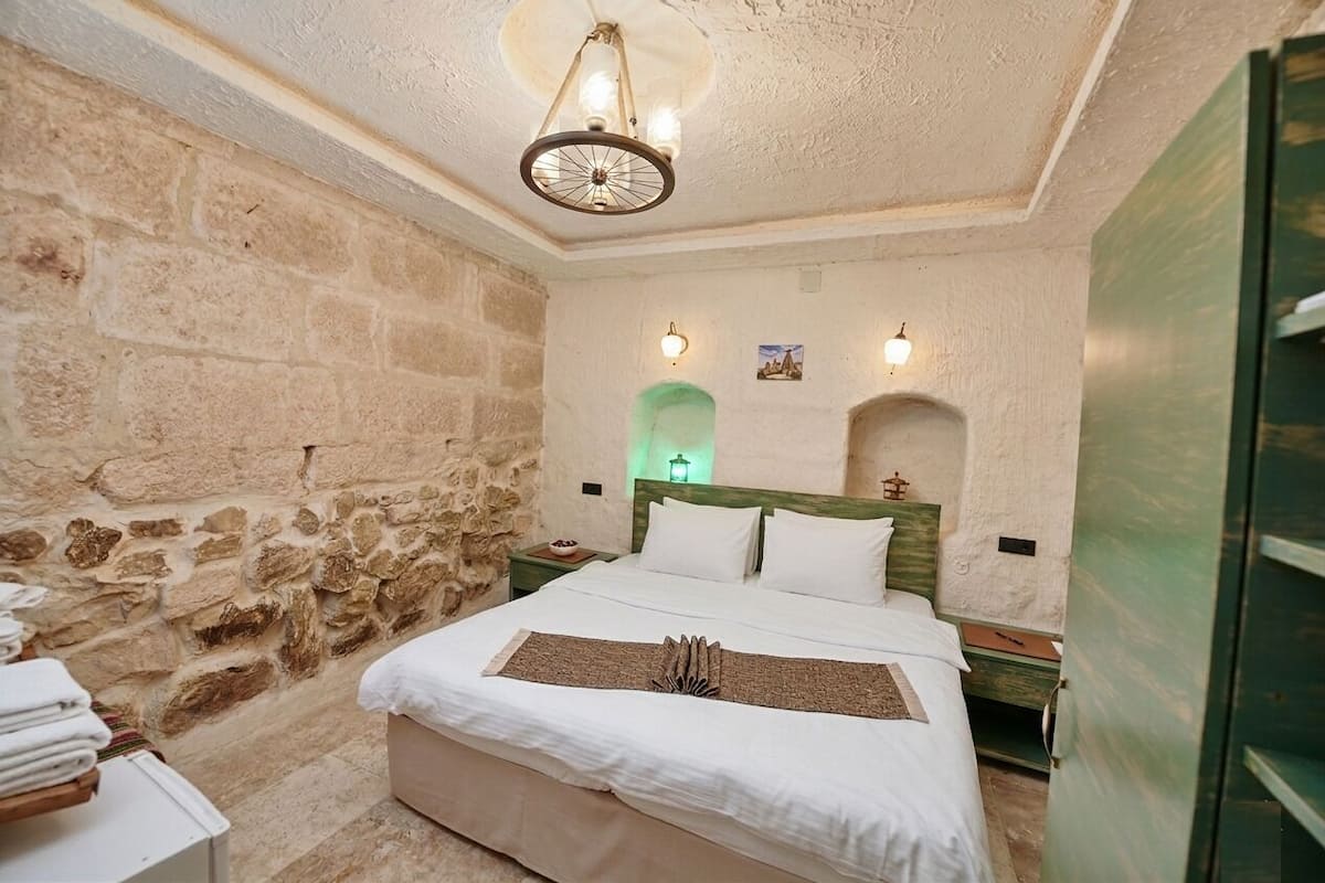 Ein Schlafzimmer mit einer Steinwand, einem Bett mit weißer Bettwäsche, einem Holz-Kopfteil und einer Wand in Grünton.