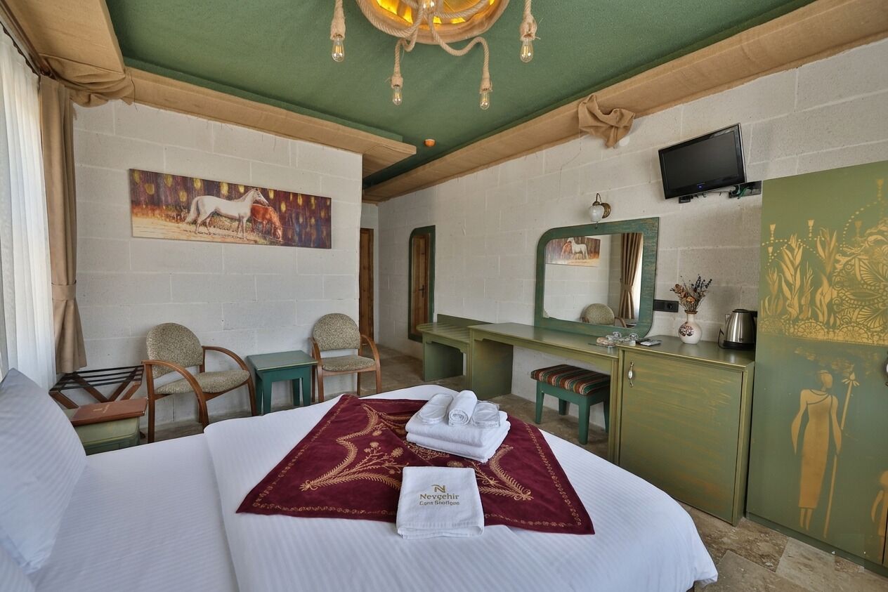 A hotel room with a bed, a desk, a chair, a television, and artwork on the walls.