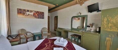 A hotel room with a bed, a desk, a chair, a television, and artwork on the walls.