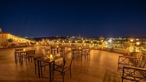 An outdoor dining area with tables and chairs, a view of the cityscape, and decorative lights. - Ashab-ı Kehf Cappadocia House (Nevsehir)