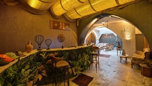 A bar area with a rustic decor, including a wooden counter and bar stools, surrounded by greenery and a textured wall. - Ashab-ı Kehf Cappadocia House (Nevsehir)