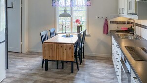 Une cuisine avec une table à manger en bois, des chaises, une fenêtre décorée de fleurs et un évier en acier inoxydable.