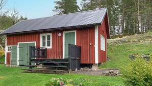 Une petite cabane en bois rouge, avec une porte verte, un petit porche et un toit en métal.
