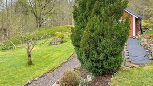 Un jardin bien entretenu, agrémenté de divers arbres, d’un chemin de gravier et d’un petit abri de jardin rouge.