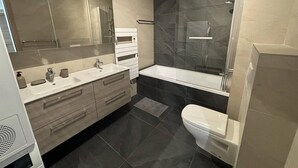 Un baño moderno con tocador doble, inodoro y zona de ducha con mampara de vidrio.