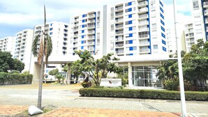 A modern apartment building with multiple balconies, a landscaped entrance area, and a clear sky.