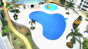 A swimming pool with a basketball court, palm trees, and a small building.