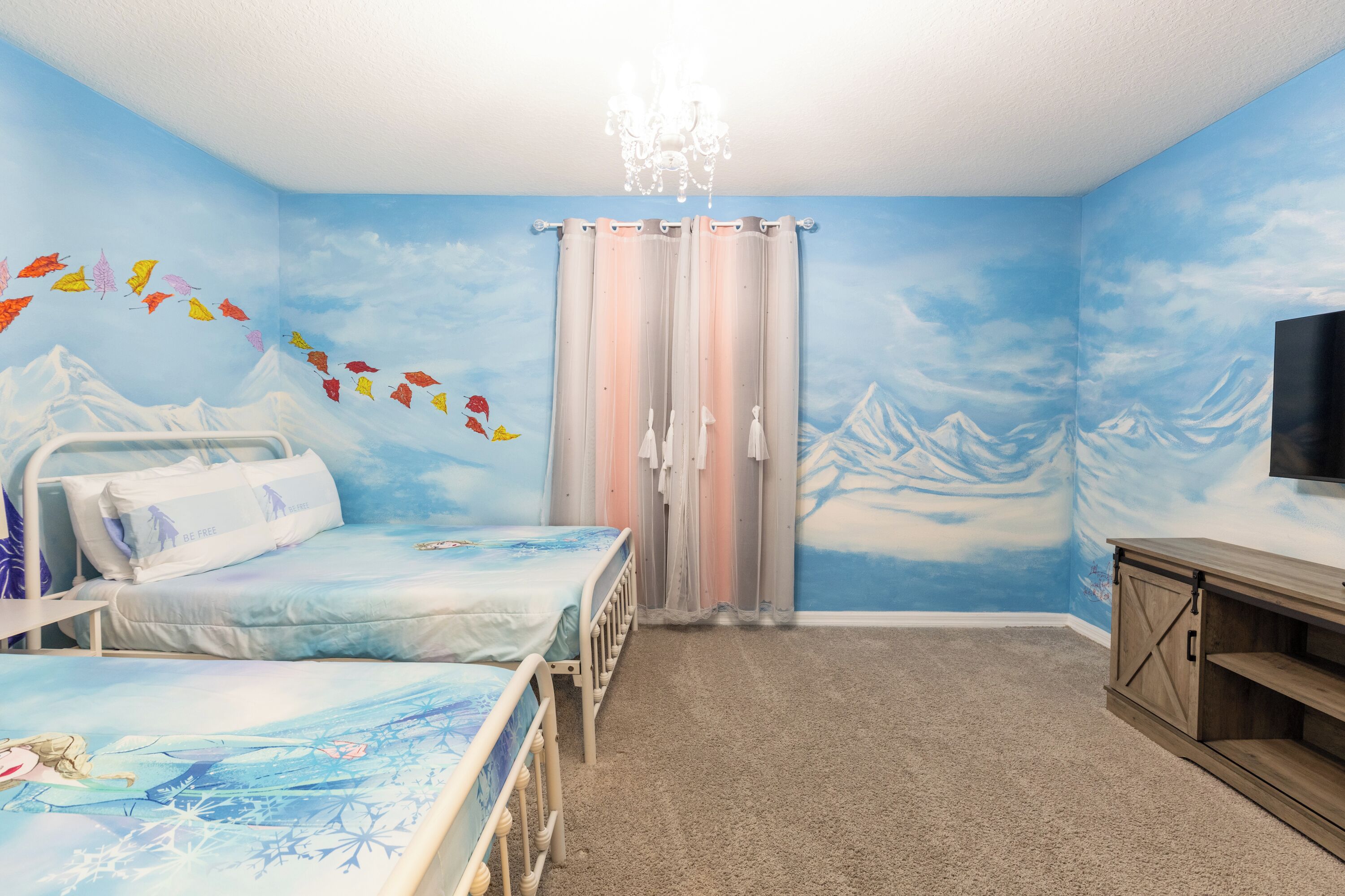 Une chambre avec deux lits, un lustre, une télévision et une fresque représentant des montagnes et des nuages.