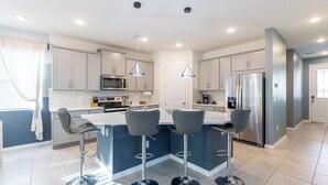 A modern kitchen with a central island, bar stools, stainless steel appliances, and pendant lighting.