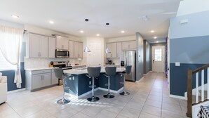 A modern kitchen with white cabinets, a central island with bar stools, stainless steel appliances, and a staircase leading to another level.