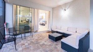 An outdoor seating area with a sofa and chairs, a glass door leading to a covered patio, and a wall-mounted light fixture.