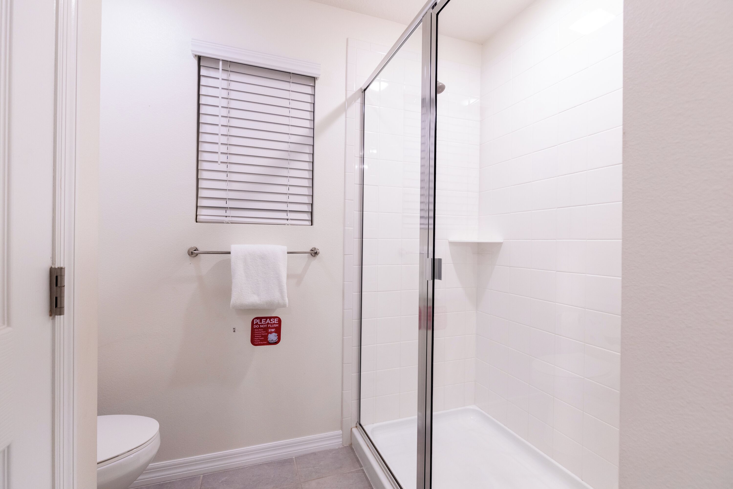 Un baño con inodoro, cabina de ducha de vidrio y ventana con persianas.