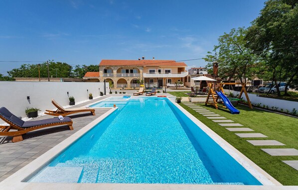 A swimming pool with lounge chairs, a slide, and a building in the background.