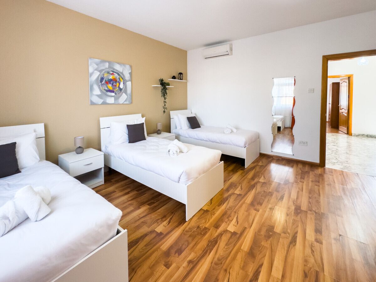 Hotellihuone, jossa on kolme sänkyä, puulattia, seinällä taulu ja peili, joka heijastaa huonetta.