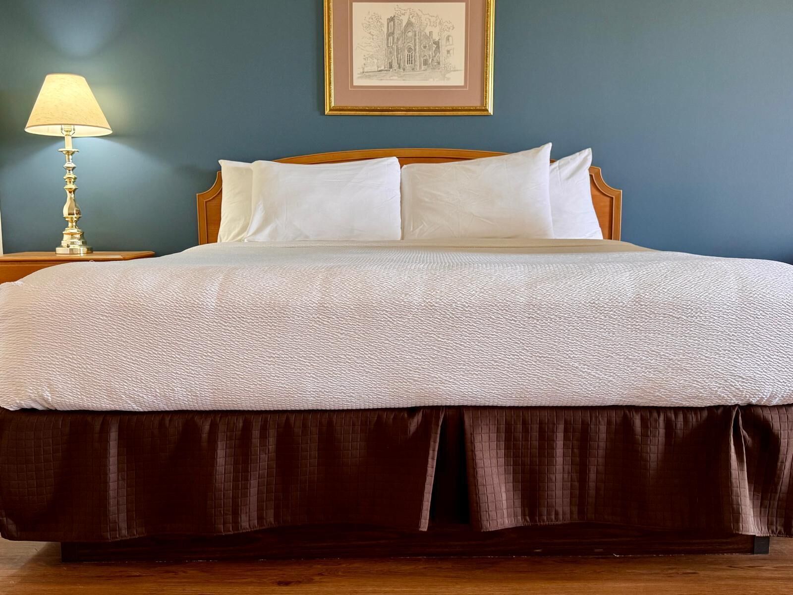 A neatly made bed with a wooden headboard, a white duvet, and a brown skirted bed base.
