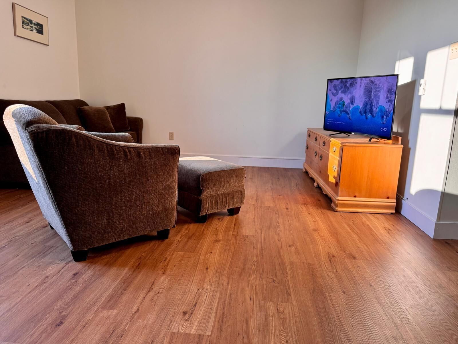 Una sala de estar con un sofá marrón, un mueble de madera con un televisor y piso de madera.