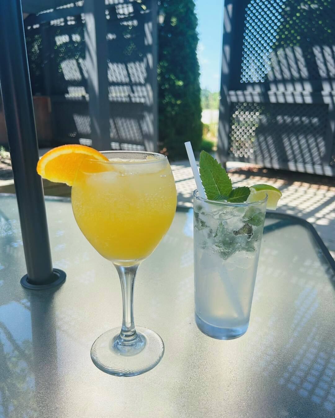 Two drinks on a table outside, one in a glass and one in a tall glass with a straw.
