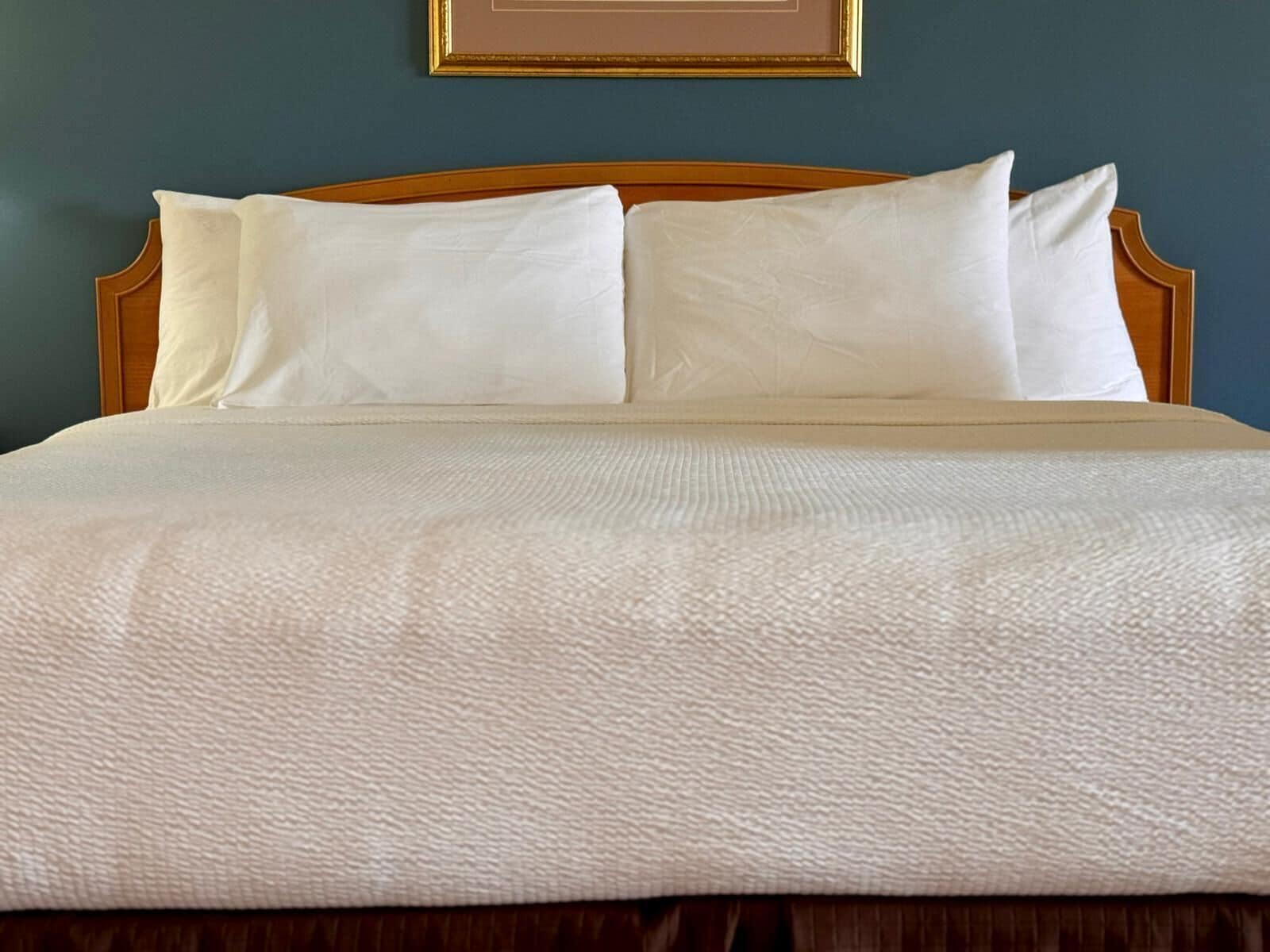 Una cama bien hecha con cabecera de madera, ropa de cama blanca y un cuadro enmarcado encima.