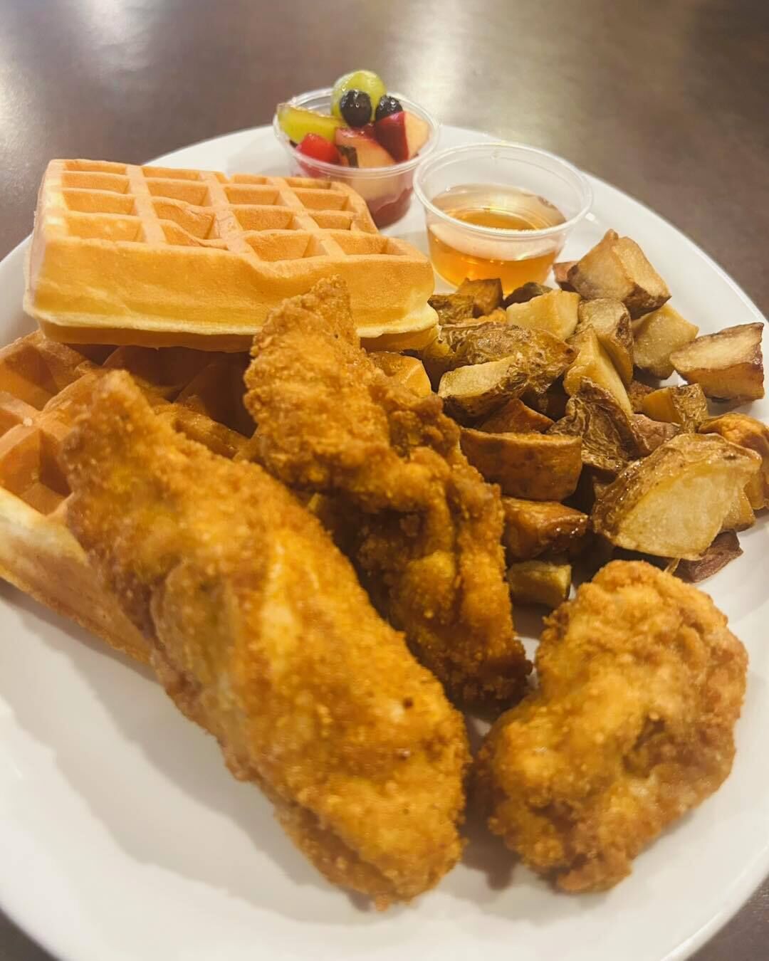 Un plato con pollo frito, gofres y una guarnición de patatas asadas.
