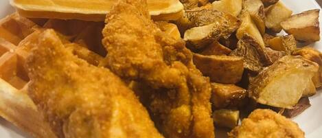 Un plato con pollo frito, gofres y una guarnición de patatas asadas.