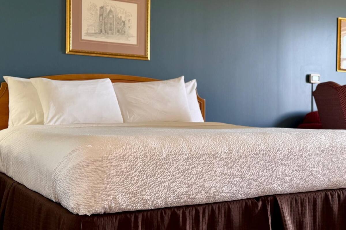 Una cama bien hecha con sábanas blancas y una base con falda marrón.