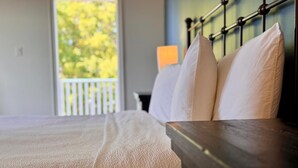 A neatly made bed with white linens and a wooden headboard in a room with a view of trees through a window. - Stone Willow Inn (St. Mary's)