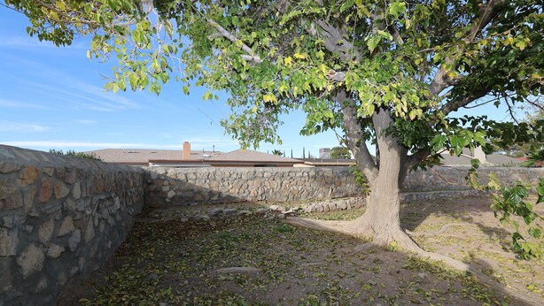 Un muro de piedra con un árbol frente a un edificio de techo rojo.