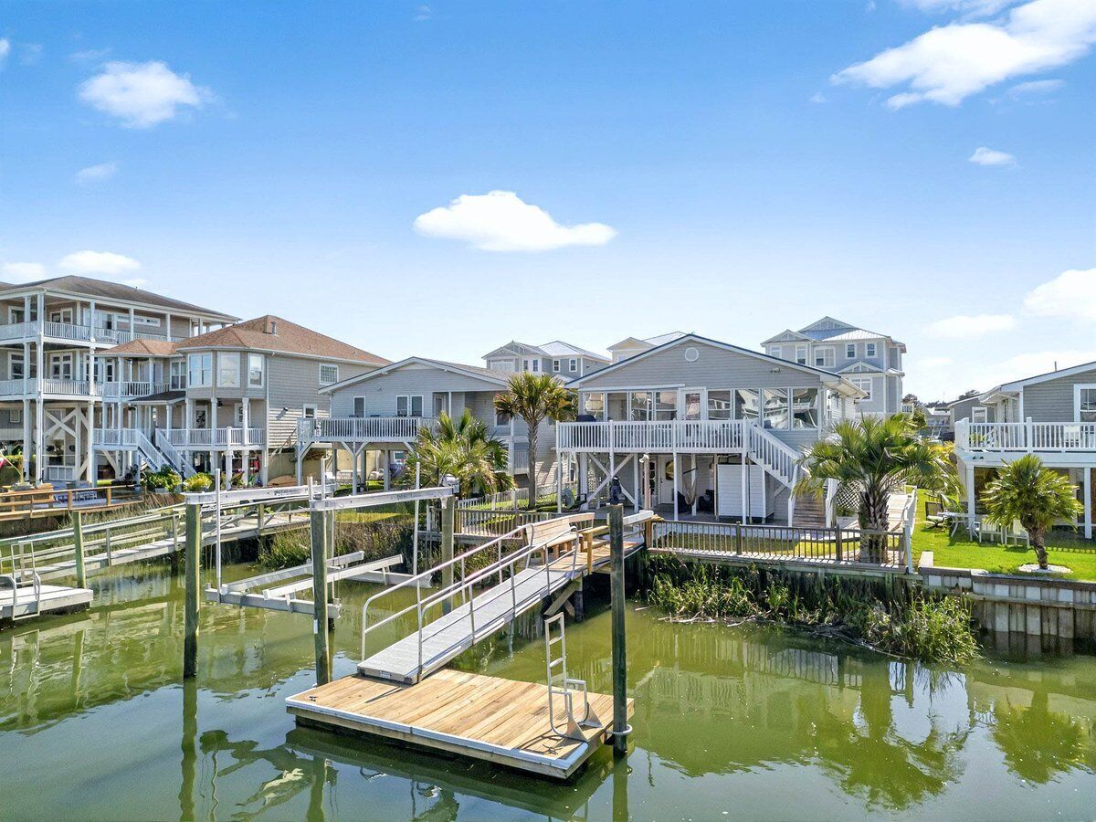 A marina with docked boats, a wooden dock, and a building with multiple balconies and a covered area.