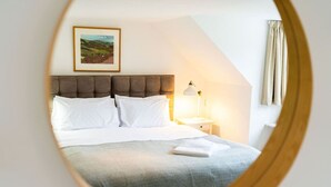 Une chambre à coucher avec un lit, une table de chevet, une lampe, un tableau encadré au mur et une fenêtre avec des rideaux.