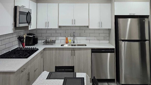 Una cocina moderna con armarios blancos, electrodomésticos de acero inoxidable y un comedor con mesa y sillas.