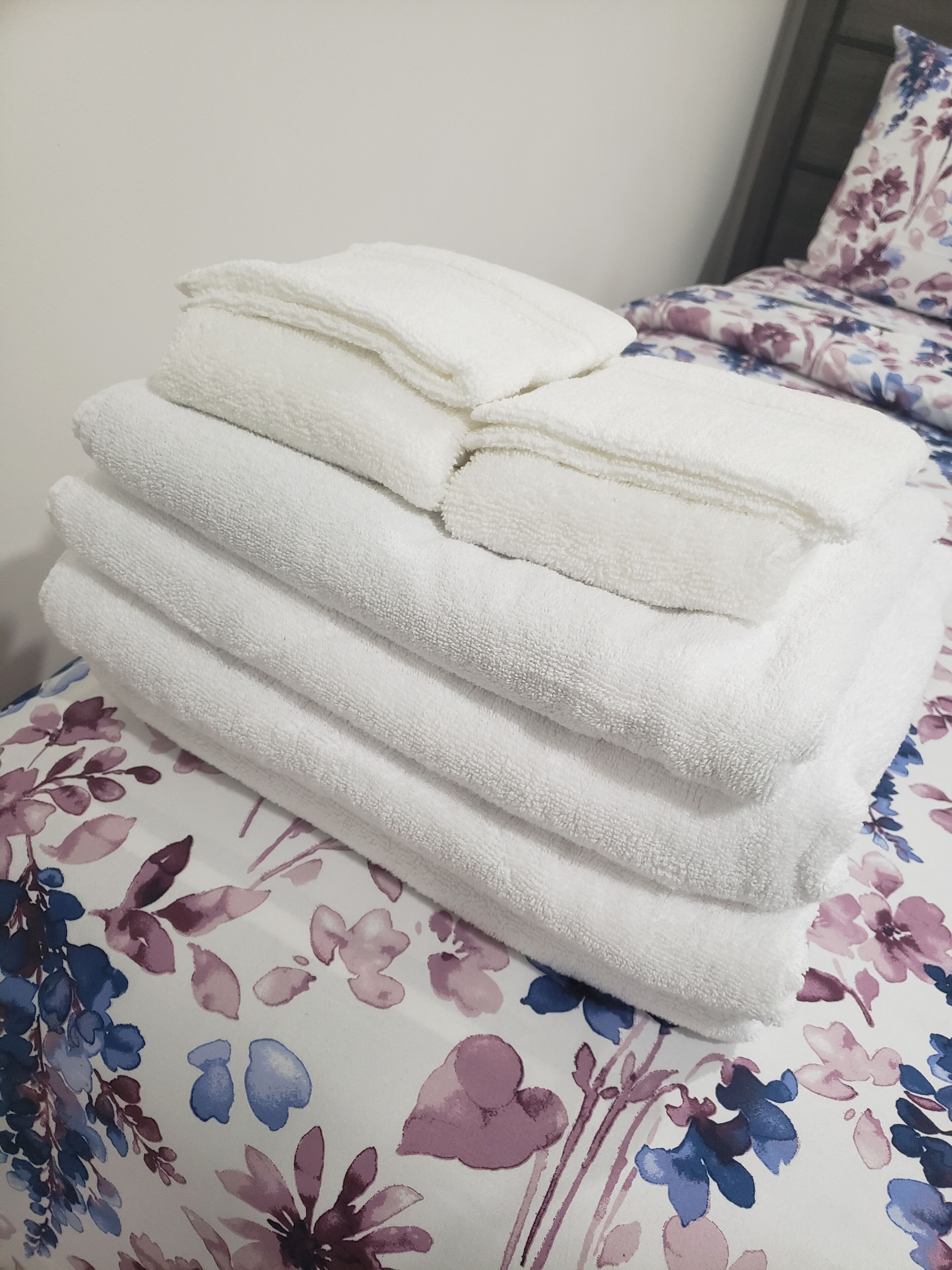 Un montón de toallas blancas dobladas cuidadosamente sobre una cama con una colcha estampada con motivos florales.