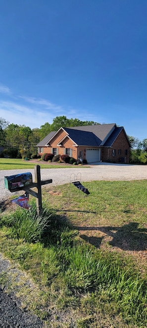 A two-story house with a garage, surrounded by a gravel driveway and a grassy lawn. - Cozy & quiet 1 Bedroom apartment with pool table and big screen TV.  (Appomattox)