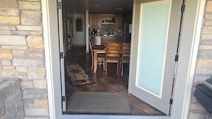 A cabin entrance with a stone wall, a wooden ceiling, a welcome sign, a kitchen area with cabinets and a dining table, and a doormat. - DISCOUNTS BOOK NOW! Beautiful 2 Bedroom Cabin with Great Views! (Island Park)