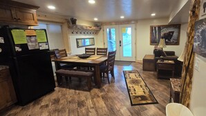 A kitchen with wooden cabinets, a black refrigerator, a dining table with chairs, a bench, and a rug. There are wooden walls, a mirror, and a door leading outside. - DISCOUNTS BOOK NOW! Beautiful 2 Bedroom Cabin with Great Views! (Island Park)