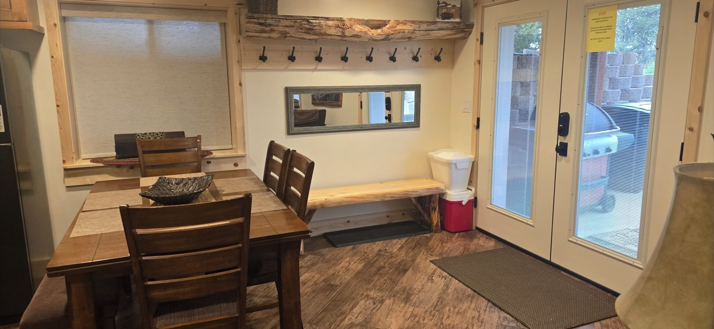 Un comedor con mesa y sillas de madera, un banco, un ventanal con vistas y una puerta con un cartel de 'STOP'.