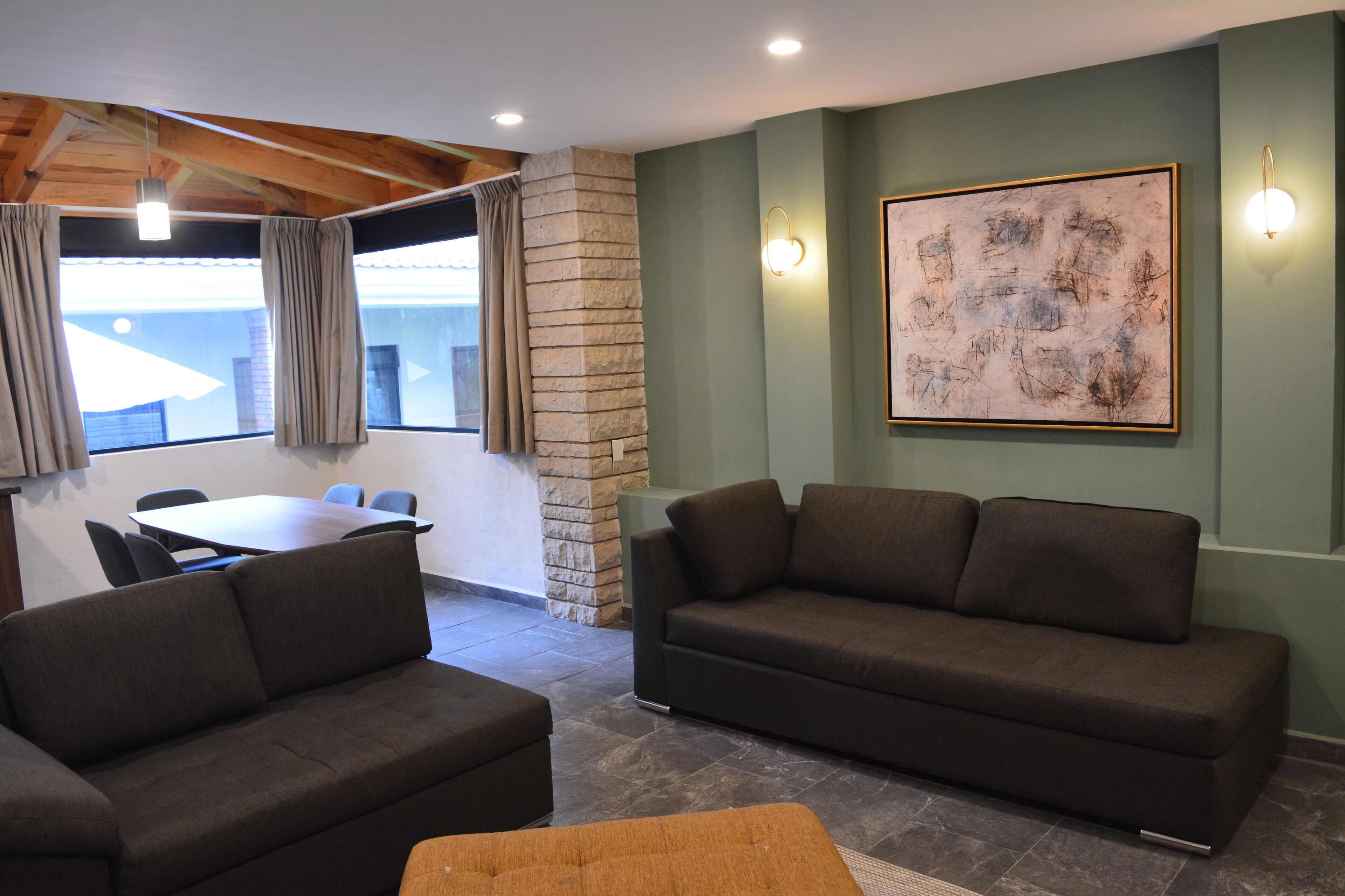 Un salon moderne avec un mur d’accent en pierre, une grande peinture abstraite et un coin repas comprenant une table et des chaises.