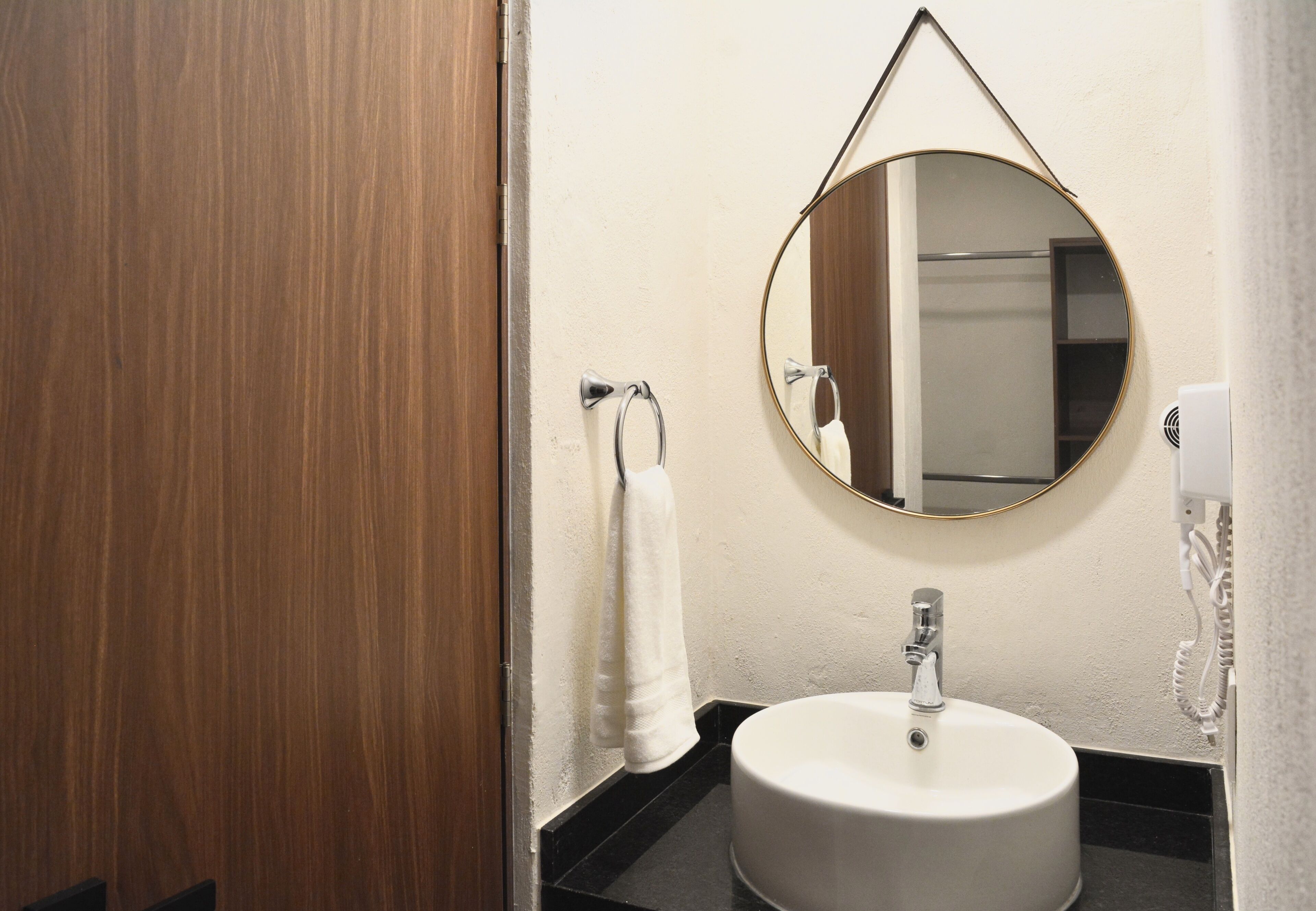 A bathroom with a round mirror, a white sink, and a towel hanging on a hook.
