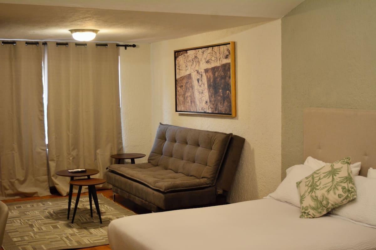 A hotel room with a bed, a sofa, a small table, and a painting on the wall.