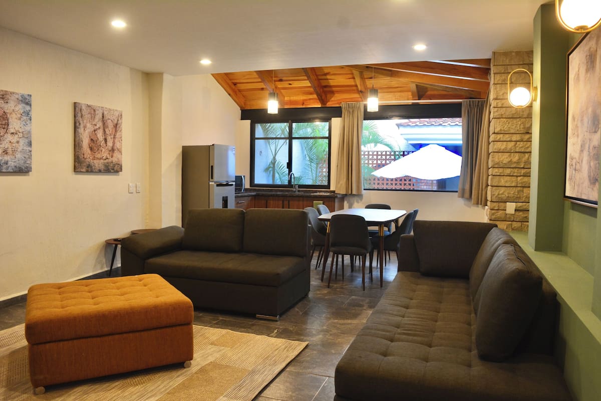 A living room with a sofa, ottoman, and dining area with chairs and a table.