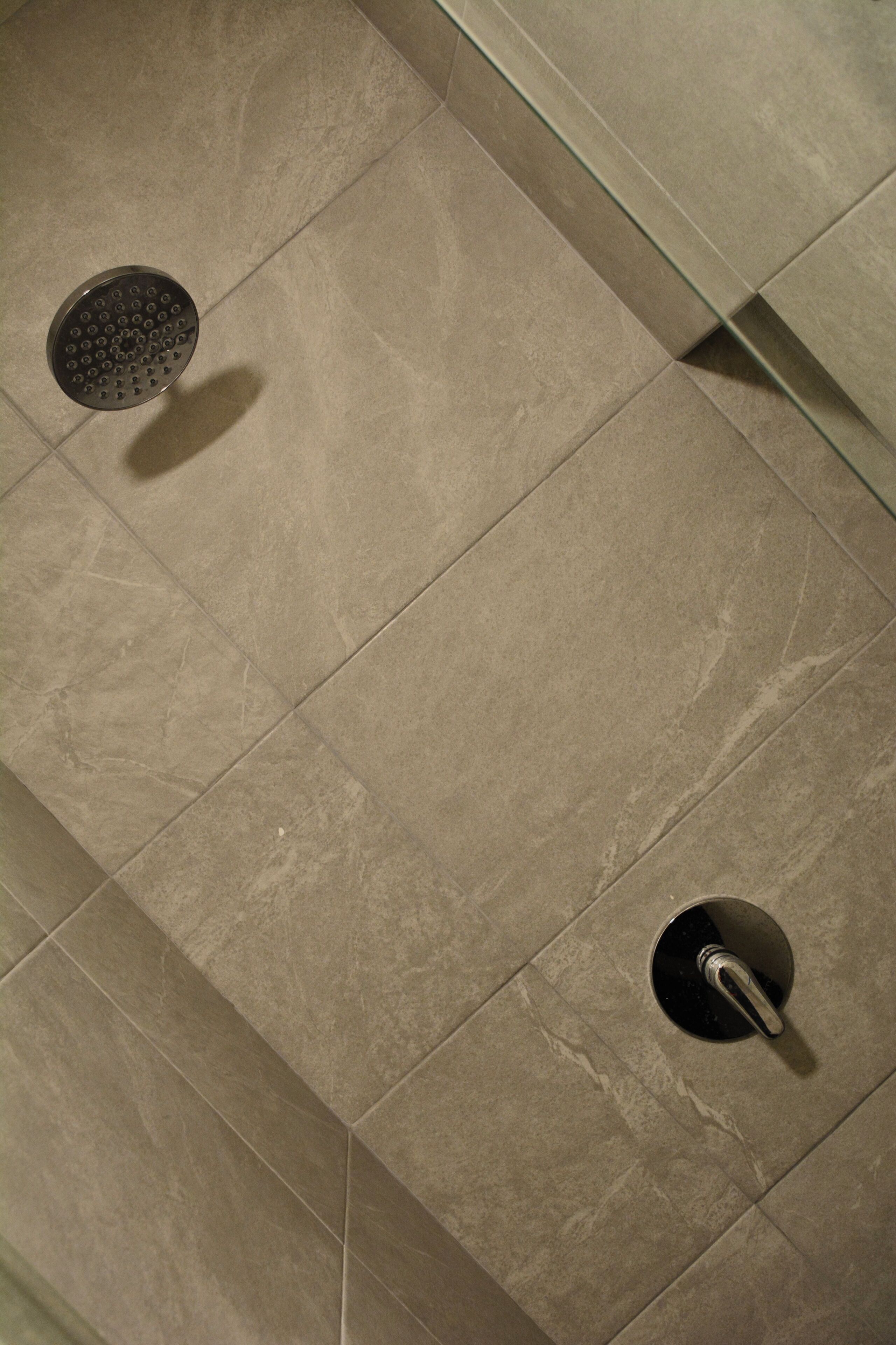 A bathroom with a shower area featuring a round showerhead and a wall-mounted faucet.