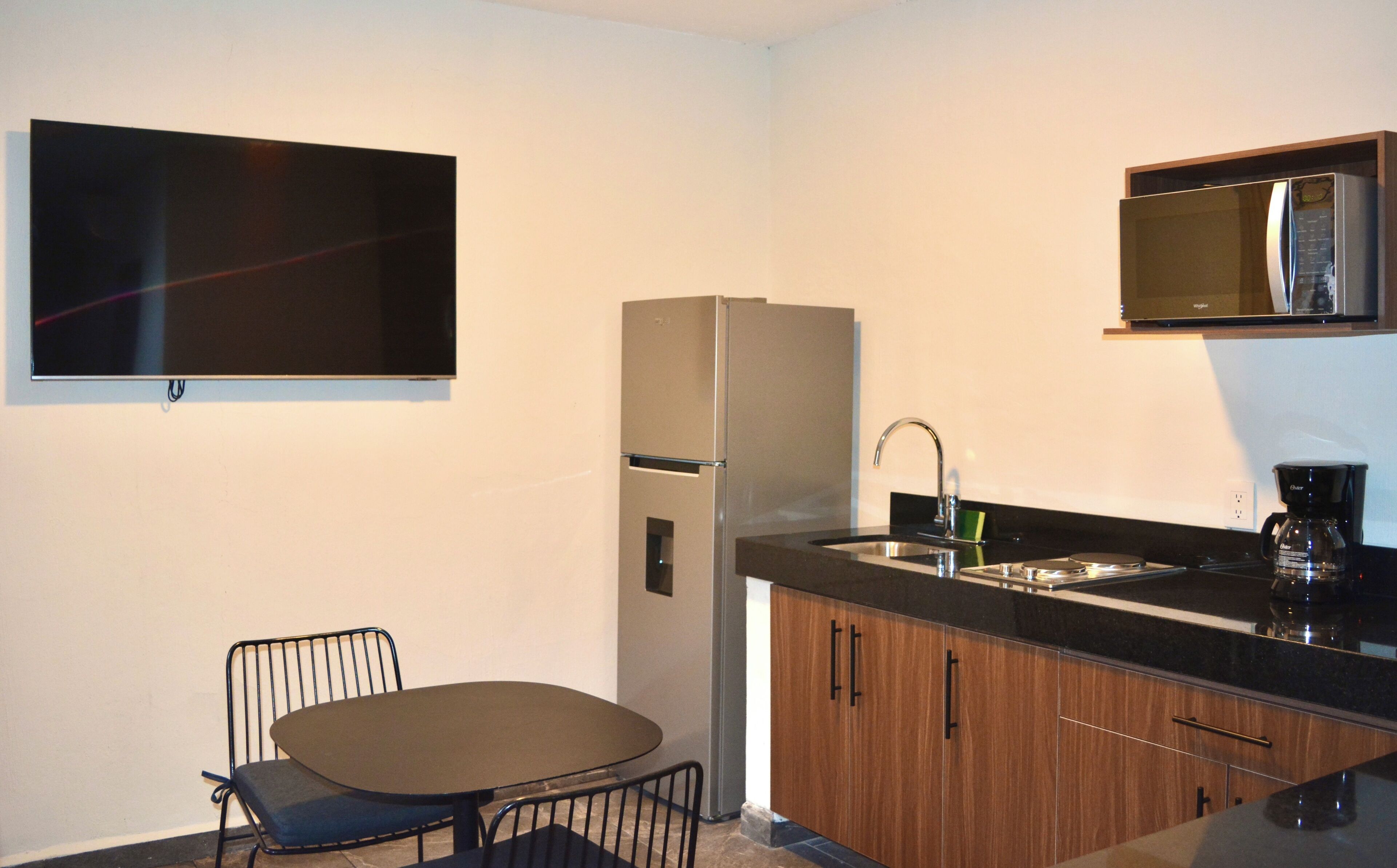 A compact kitchen with a refrigerator, a sink, a coffee maker, and a dining area with a chair and table.