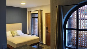 Una camera da letto con un letto, una finestra con tende, una porta e vista su un muro di mattoni.