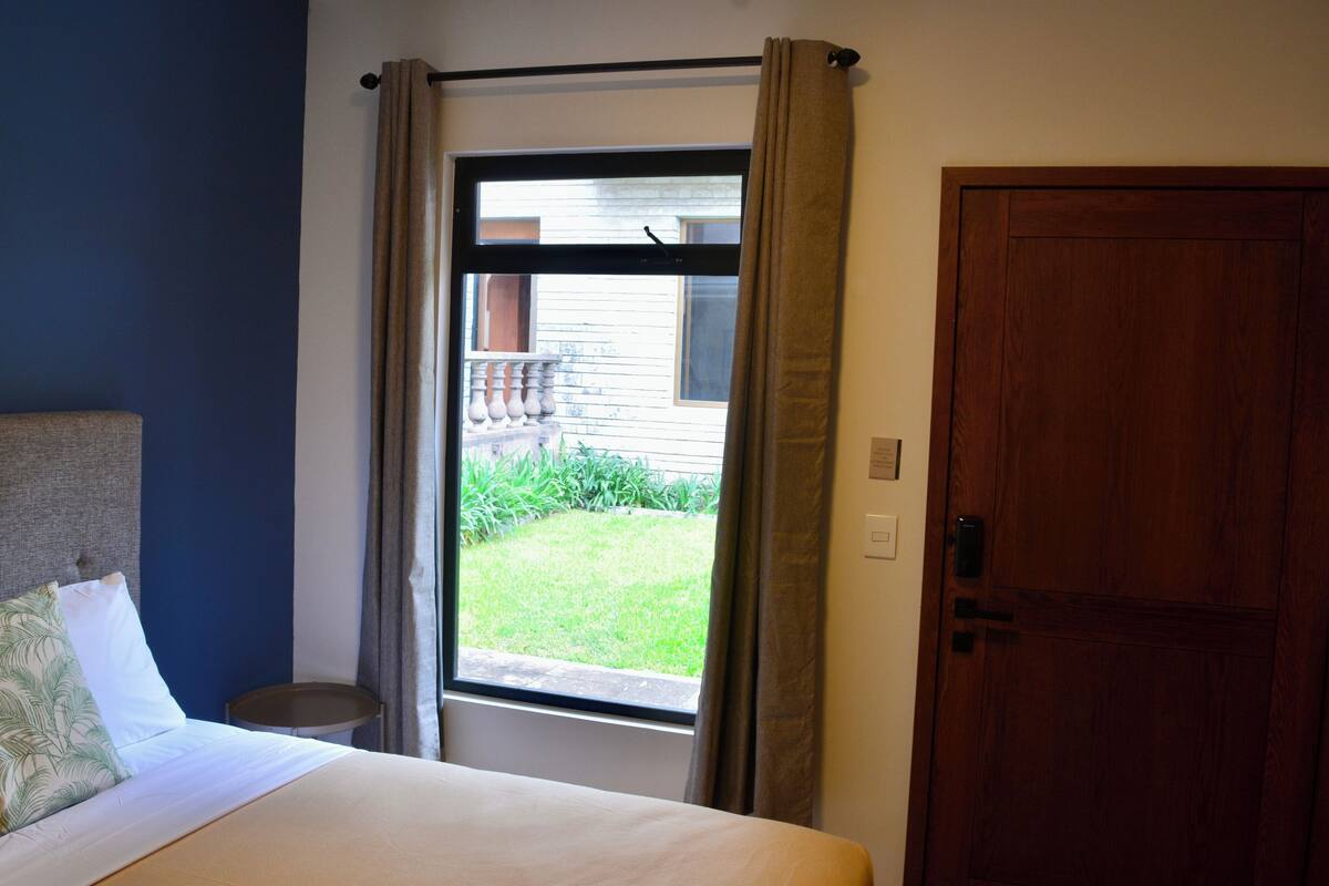 A hotel room with a bed, a small round table, a window with curtains, and a wooden door.