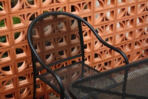 A metal chair with a mesh backrest and a metal table, positioned in front of a brick wall with a geometric pattern. - Casa Palmas (Zapopan)