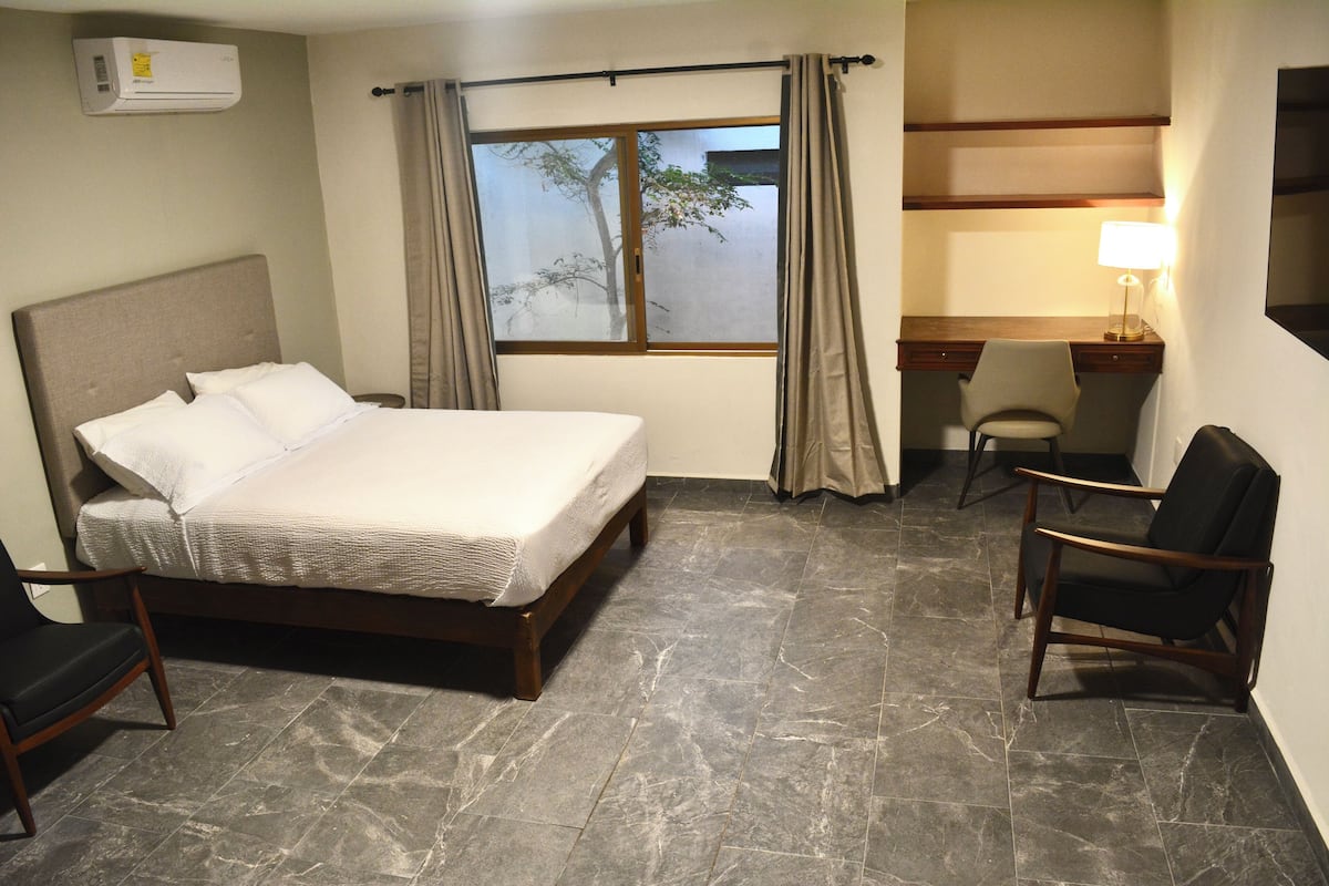 A hotel room with a bed, a desk, a chair, and a window with curtains.