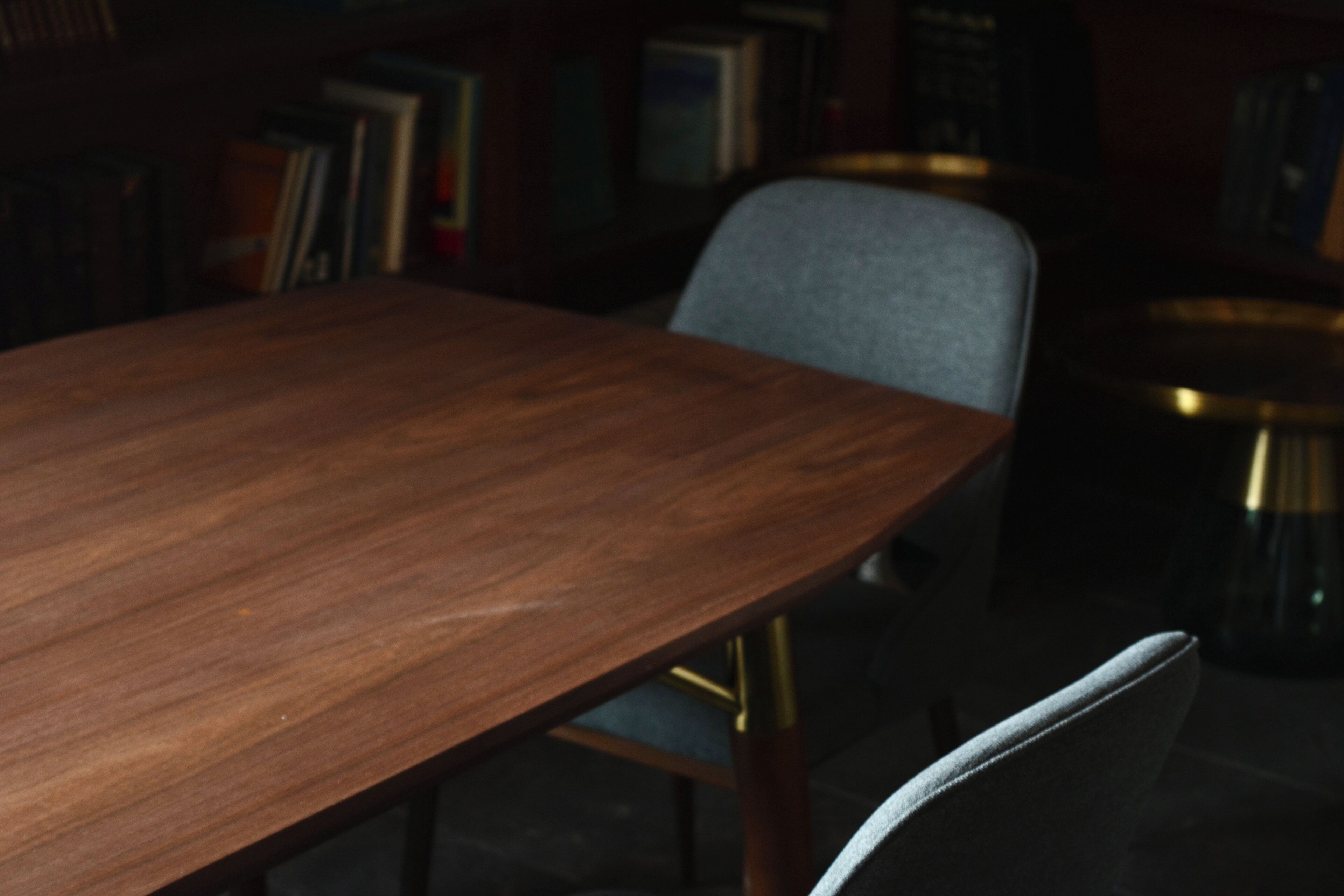 Una mesa de madera con una silla en una habitación tenuemente iluminada, con estanterías de libros al fondo.
