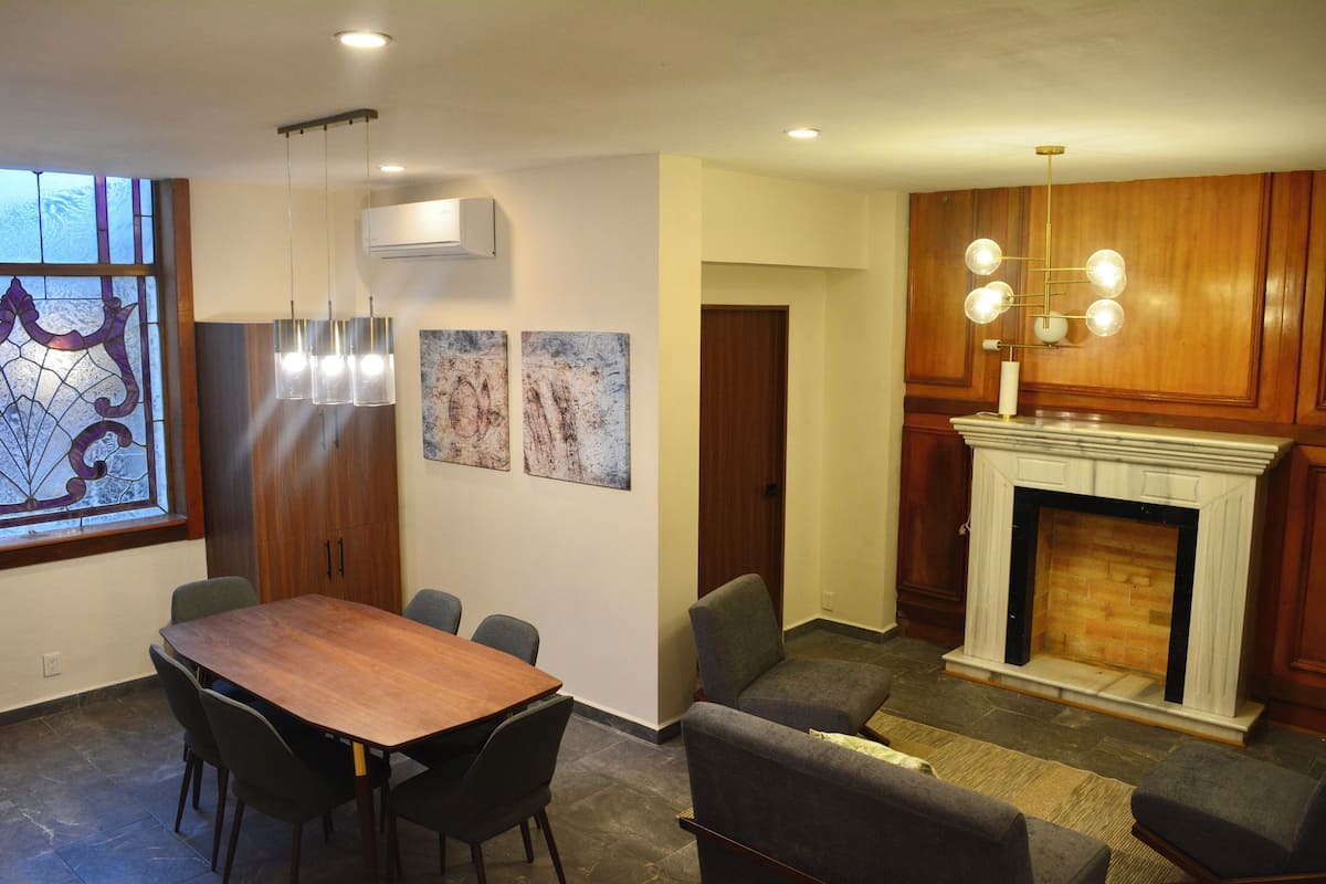A dining area with a wooden table and chairs, a fireplace with a white mantel, and a stained glass window.