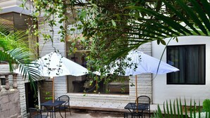 Patio esterno con due tavoli e sedie, immerso nel verde e ombrelloni bianchi.