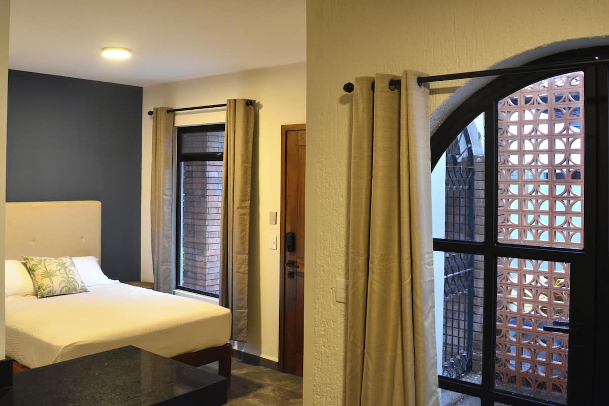 A hotel room with a bed, a small table, and a window with curtains.