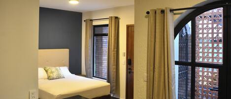 A hotel room with a bed, a small table, and a window with curtains.